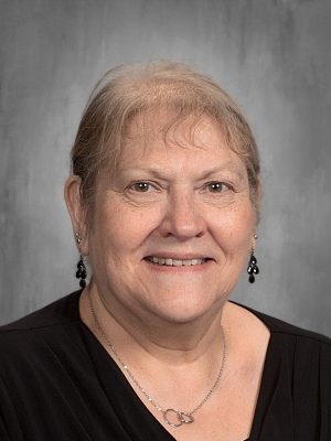 Portrait of Danna Powers, smiling woman with short gray hair, wearing a black top and silver necklace.