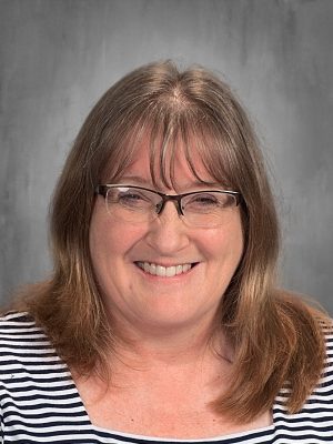Portrait of Cindy Smith, smiling and wearing glasses, against a gray background.